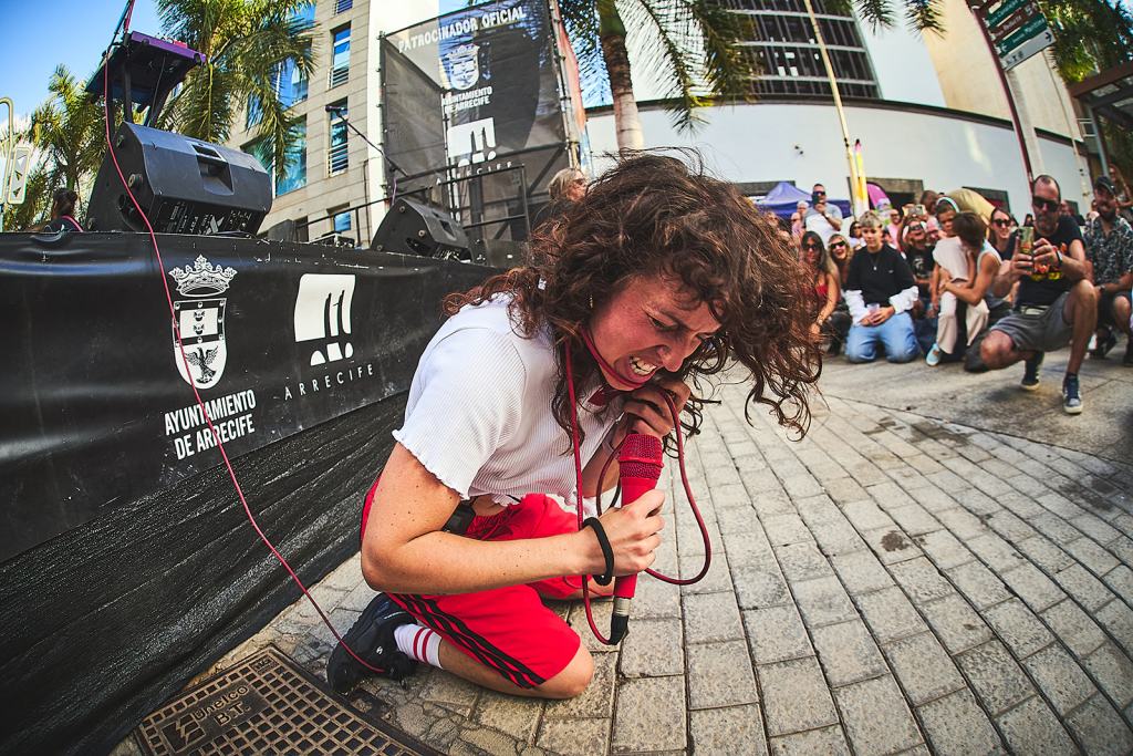 A passionate performer on stage, kneeling while holding a microphone and singing energetically, with an audience of enthusiastic spectators in the background.