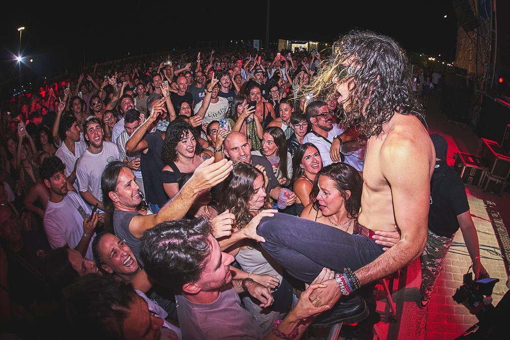 A lively concert scene with a lead singer interacting with enthusiastic fans in the front row, surrounded by a large crowd enjoying the performance.